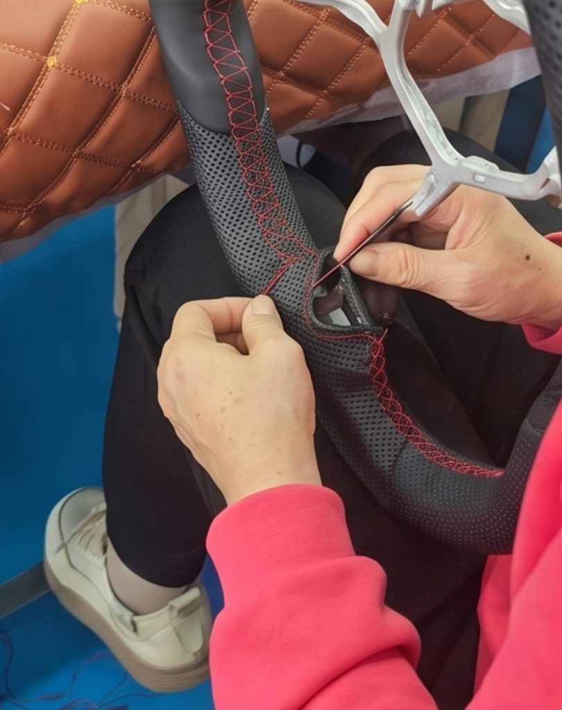 Red hand stitching being applied to a black perforated leather custom steering wheel