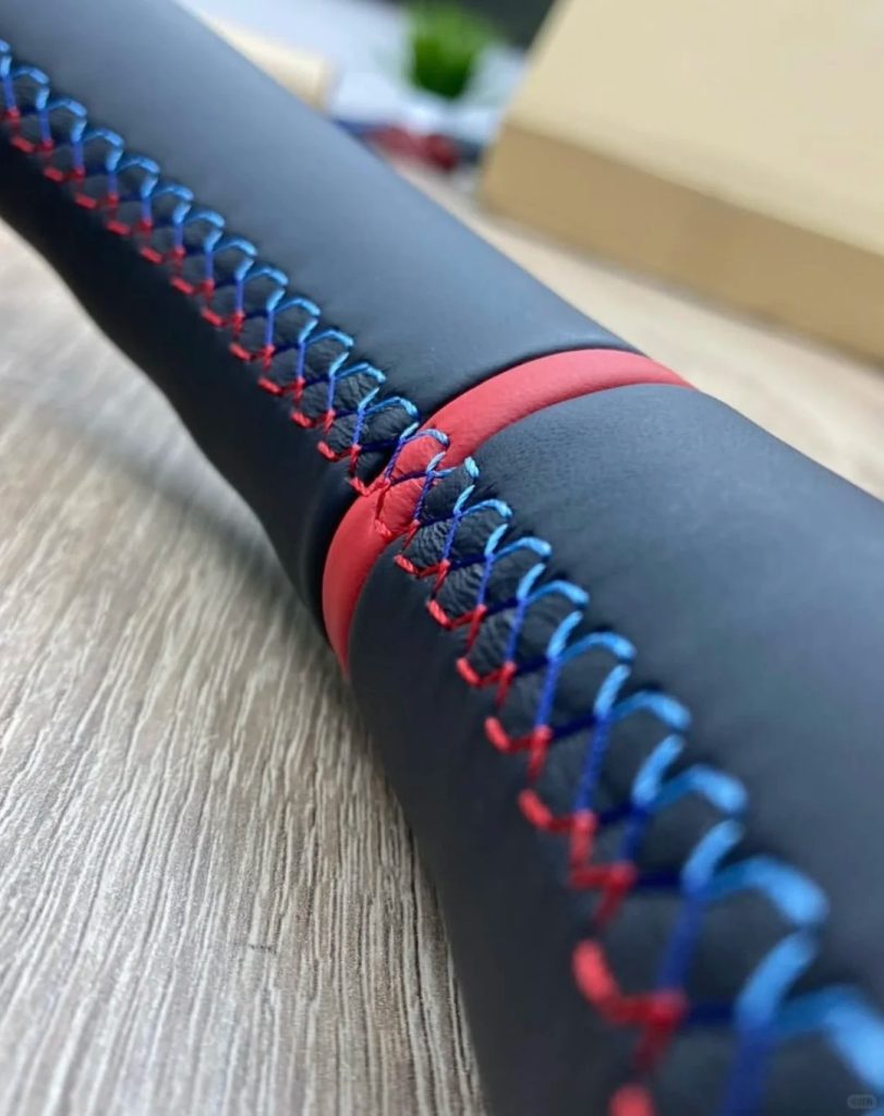 Close-up of red, blue, and dark blue stitching beside a red center marker on a black steering wheel